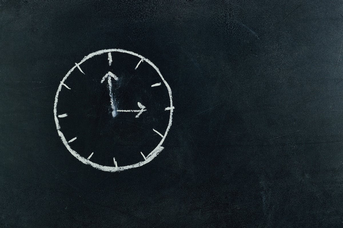 chalk drawing of a clock at 3 o'clock on a blackboard